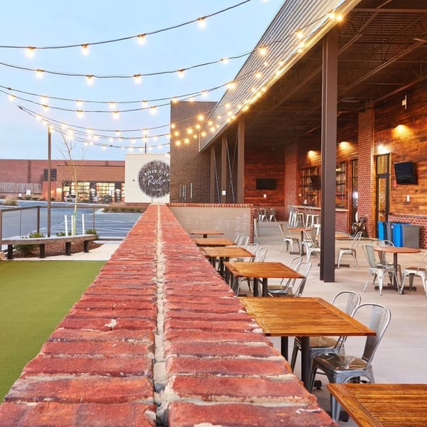 Outdoor patio of River City Roll with string lights, brick walls, wooden tables, and metal chairs.