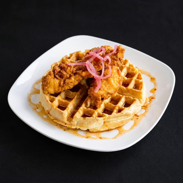 Crispy fried chicken and a waffle drizzled with syrup and topped with pickled red onions.