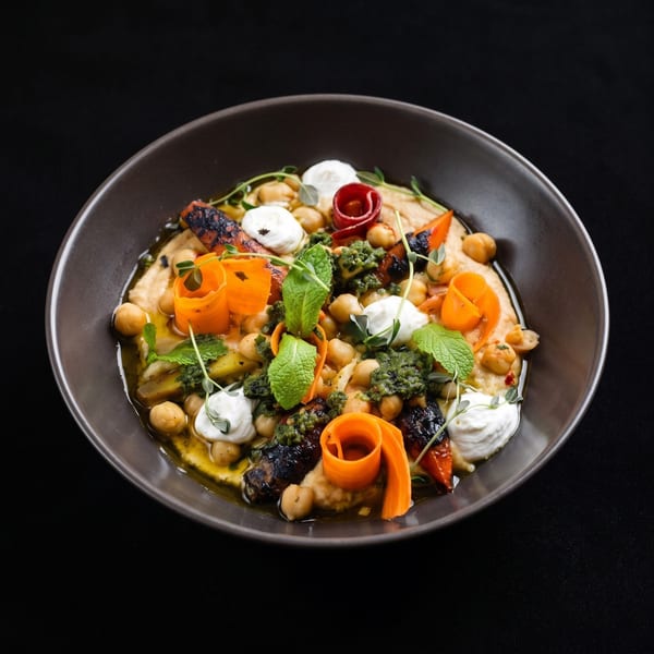 Hummus bowl with roasted carrots, chickpeas, pesto, yogurt, and fresh herbs.