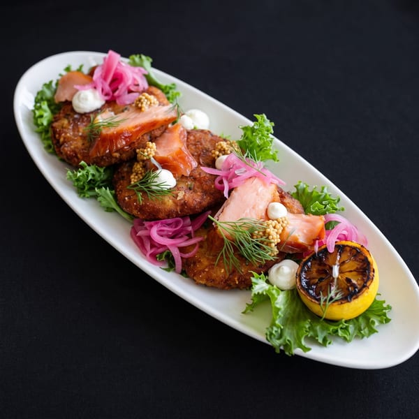 Crispy potato pancakes topped with smoked salmon, pickled onions, dill, and a grilled lemon.