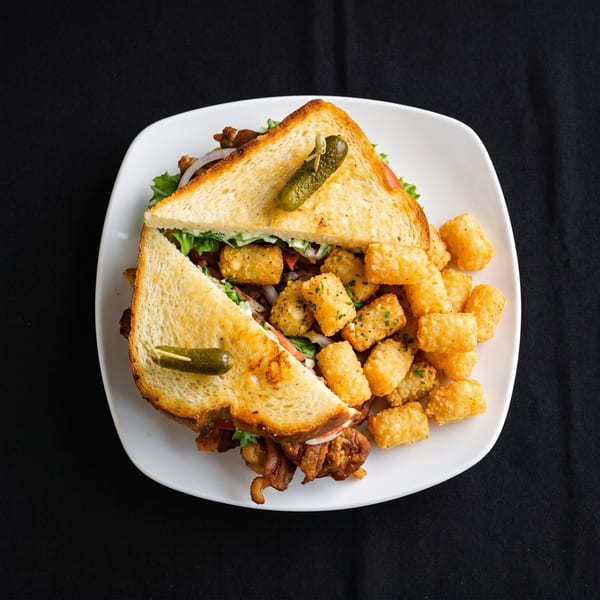 A toasted sandwich with meat, lettuce, tomato, and onion, served with a side of tater tots.